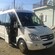 A minibus with its door open and a Mercedes Benz logo on the front is parked in front of a building